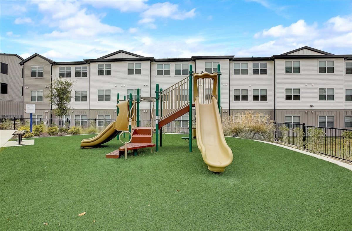 Play area featuring multiple slides, climbing platforms, and open turf space inside the courtyard.